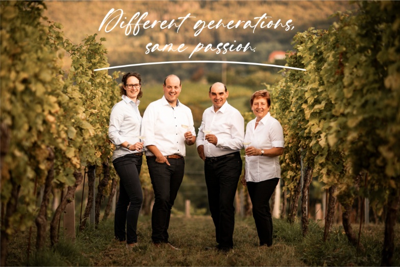 Different generations, same passion is written in white on the image. From left to right, Maria, Christoph, Josef, and Herta stand in the vineyard with a glass of white wine in hand