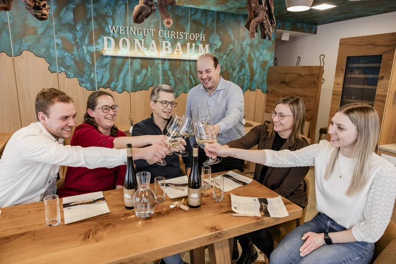 6 Personen stoßen bei einer Weinverkostung mit einem Glas Wein an.