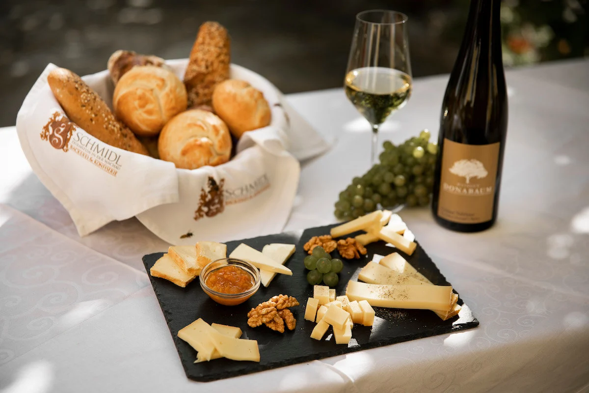 Genussvoll gedeckter Tisch mit Käseplatte, Gebäckkorb und einer Flasche Wein.