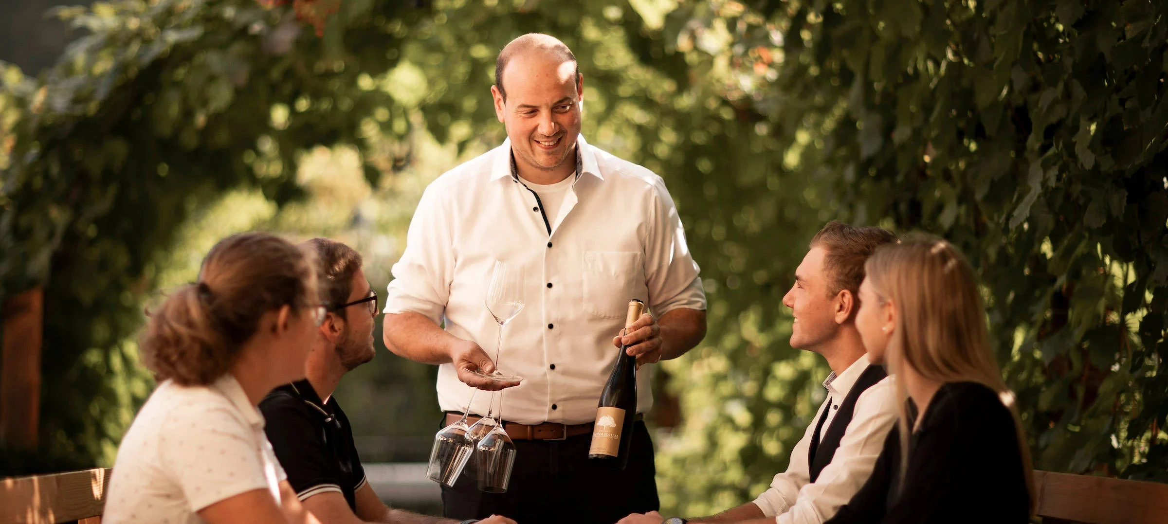Christoph serviert Wein an einem Tisch mit vier Personen